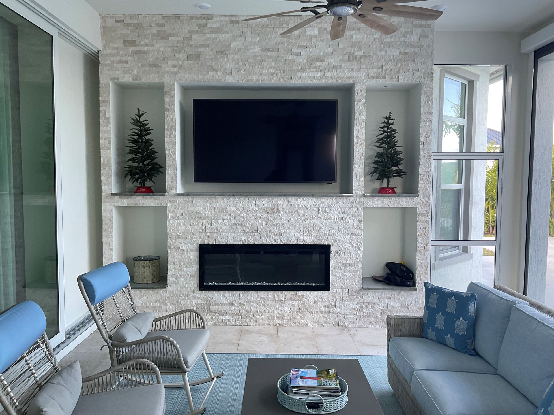 Bright living room with built-in fireplace, TV, blue chairs and sofa, and Christmas trees on shelves
