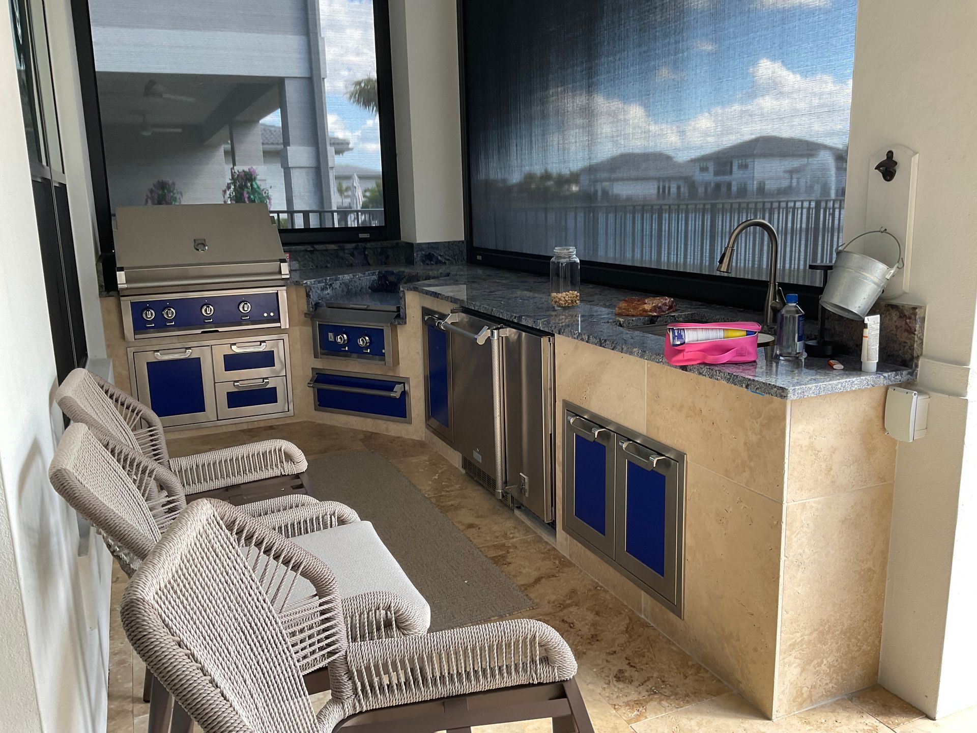 Outdoor patio with wicker chairs, built-in grill counter, and blue-trimmed cabinets overlooking water.