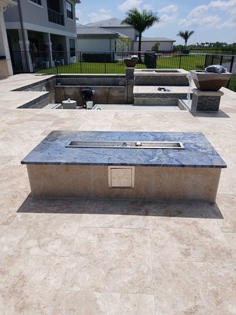 Outdoor stone barbecue grill on a patio with a pool and lawn in the background