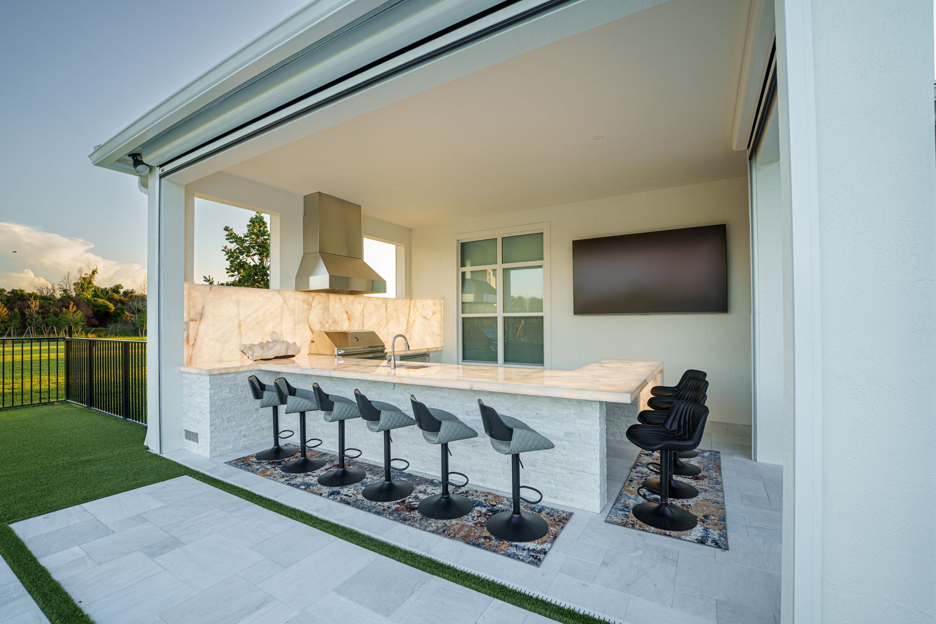 Modern outdoor kitchen with bar seating, grill, and wall-mounted TV under a covered patio