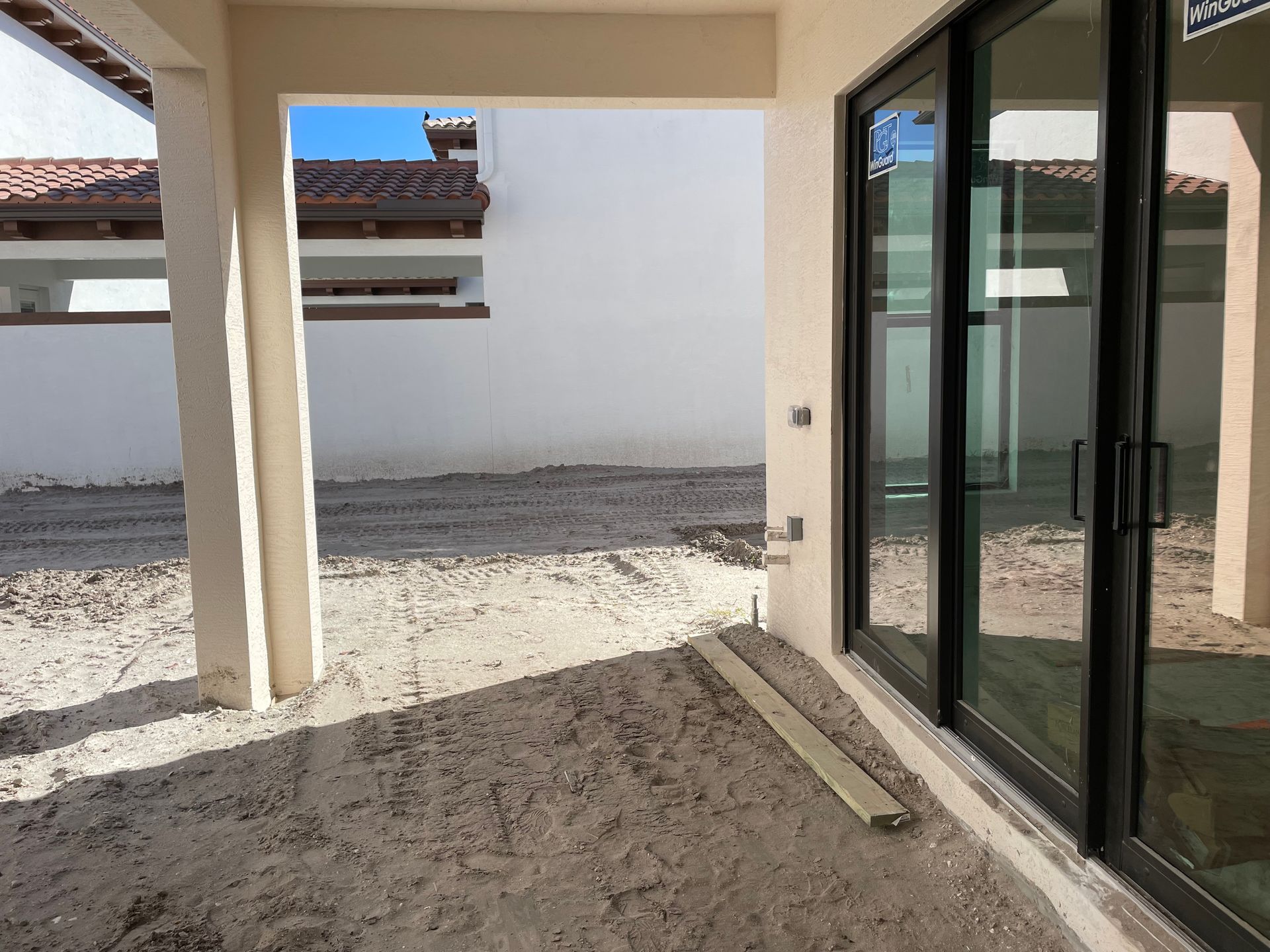 Covered patio with sliding glass doors, sandy ground, and a white courtyard wall.