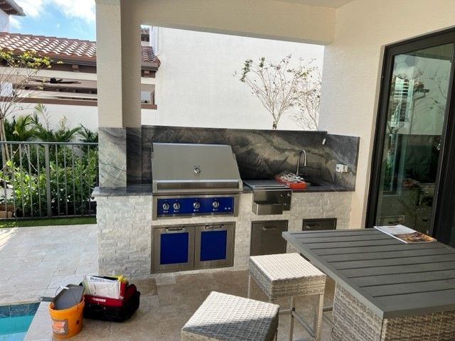 Outdoor patio with built-in grill, blue cabinet doors, and a small table beside a glass door.