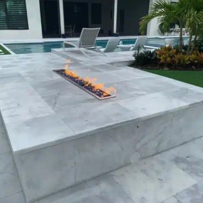 Modern patio with a linear fire pit set into a light gray concrete platform beside a pool