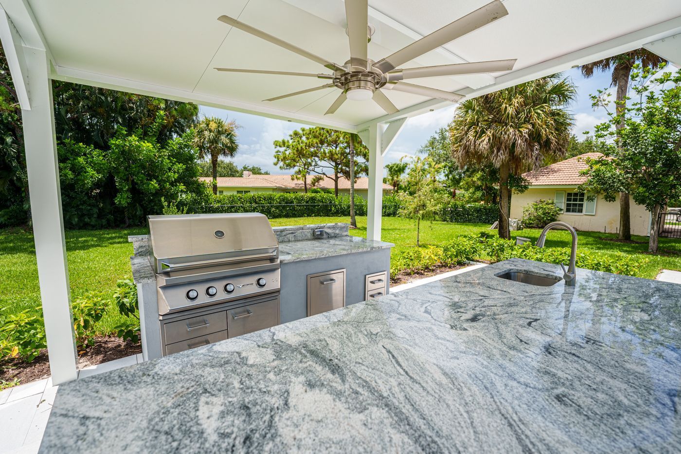 Outdoor patio with stainless grill, granite countertop, ceiling fan, and lush garden view