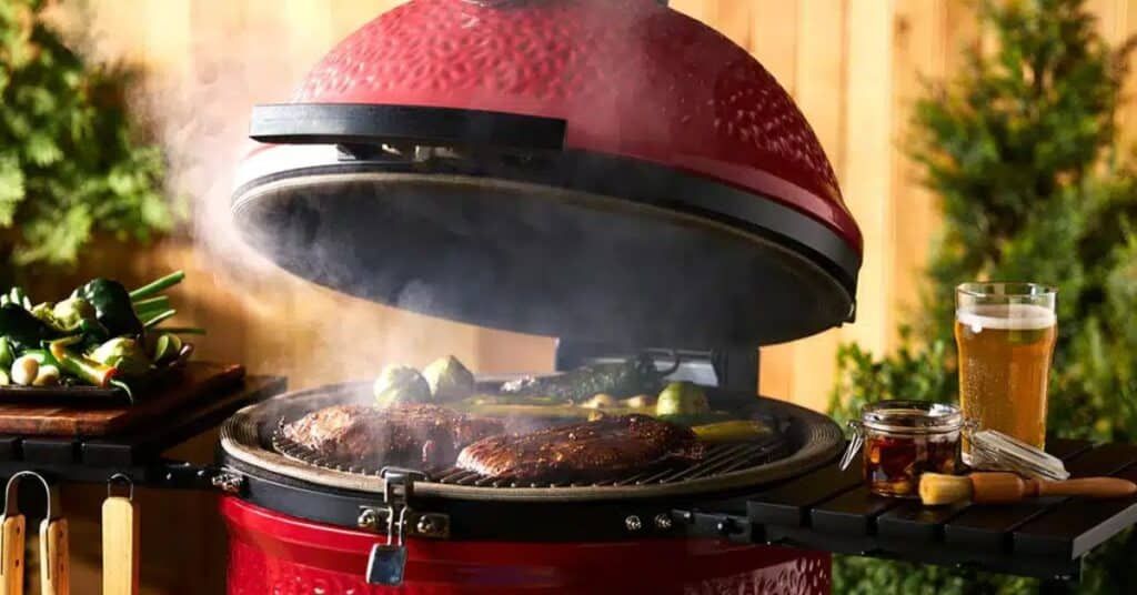 Red grill with lid open, sizzling steaks, smoke rising, and a beer on a sunny patio table