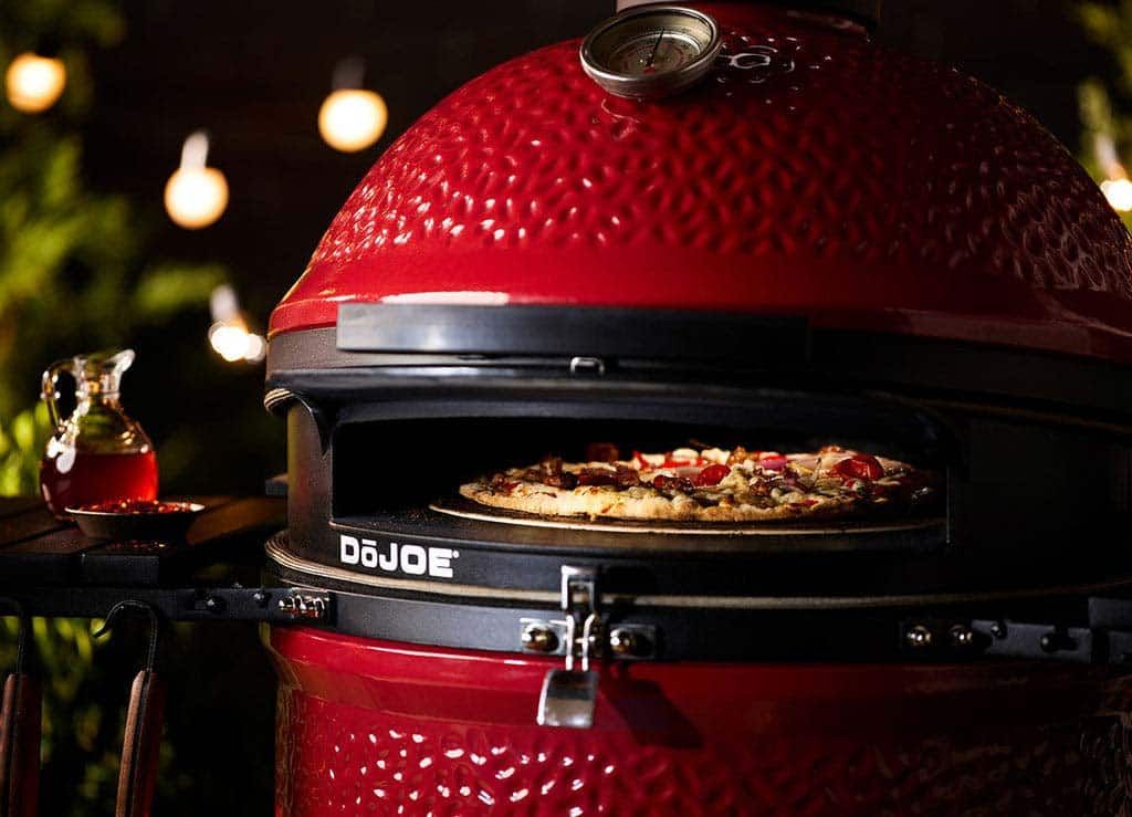 Red ceramic pizza oven with a pizza baking inside, lit warmly in a dark setting