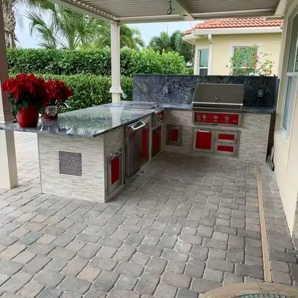 Outdoor patio with built-in stainless steel grill, red cabinets, and gray stone countertops under a covered roof