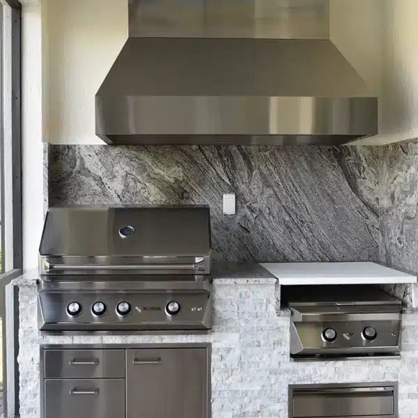 Outdoor kitchen with stainless steel grill, range hood, and marble backsplash