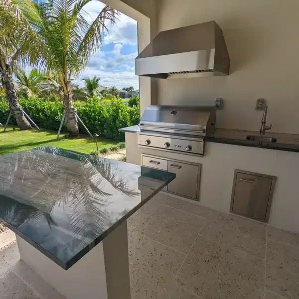 Outdoor patio kitchen with stainless grill, granite counter, and tropical garden view