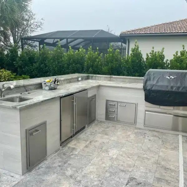 Outdoor stone patio with built-in stainless outdoor kitchen and grill under a covered gazebo.