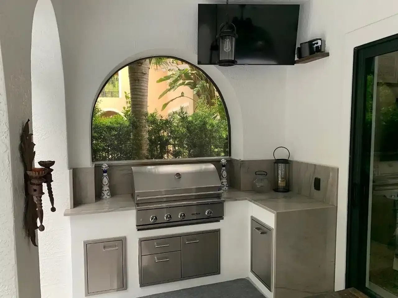 Outdoor kitchen with stainless steel grill, sink, and cabinets beside a garden view