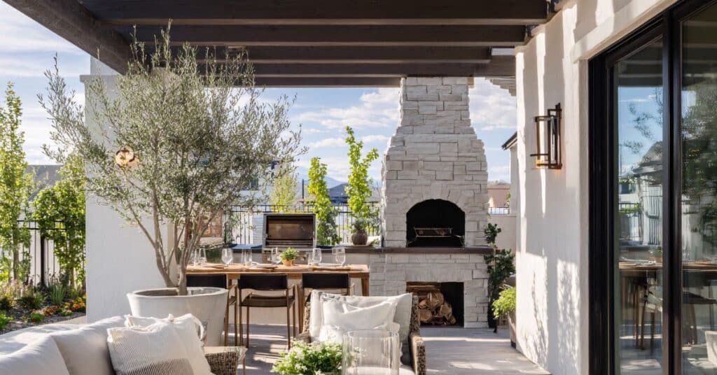 Covered patio with outdoor dining table, seating, and a built-in stone fireplace beside sliding glass doors.
