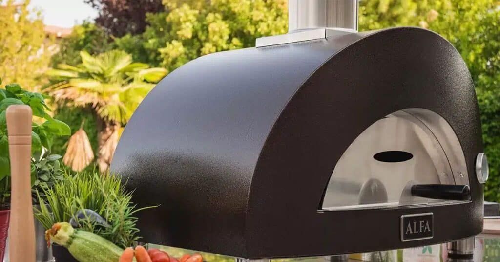 Outdoor black pizza oven on a patio with trees and greenery in the background