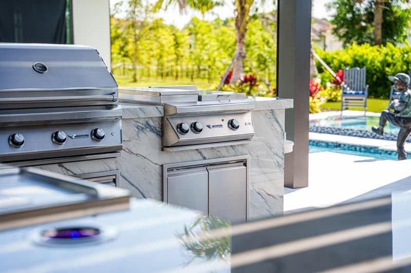 An outdoor Florida kitchen with outdoor kitchen appliances, a stainless steel grill, and a pool