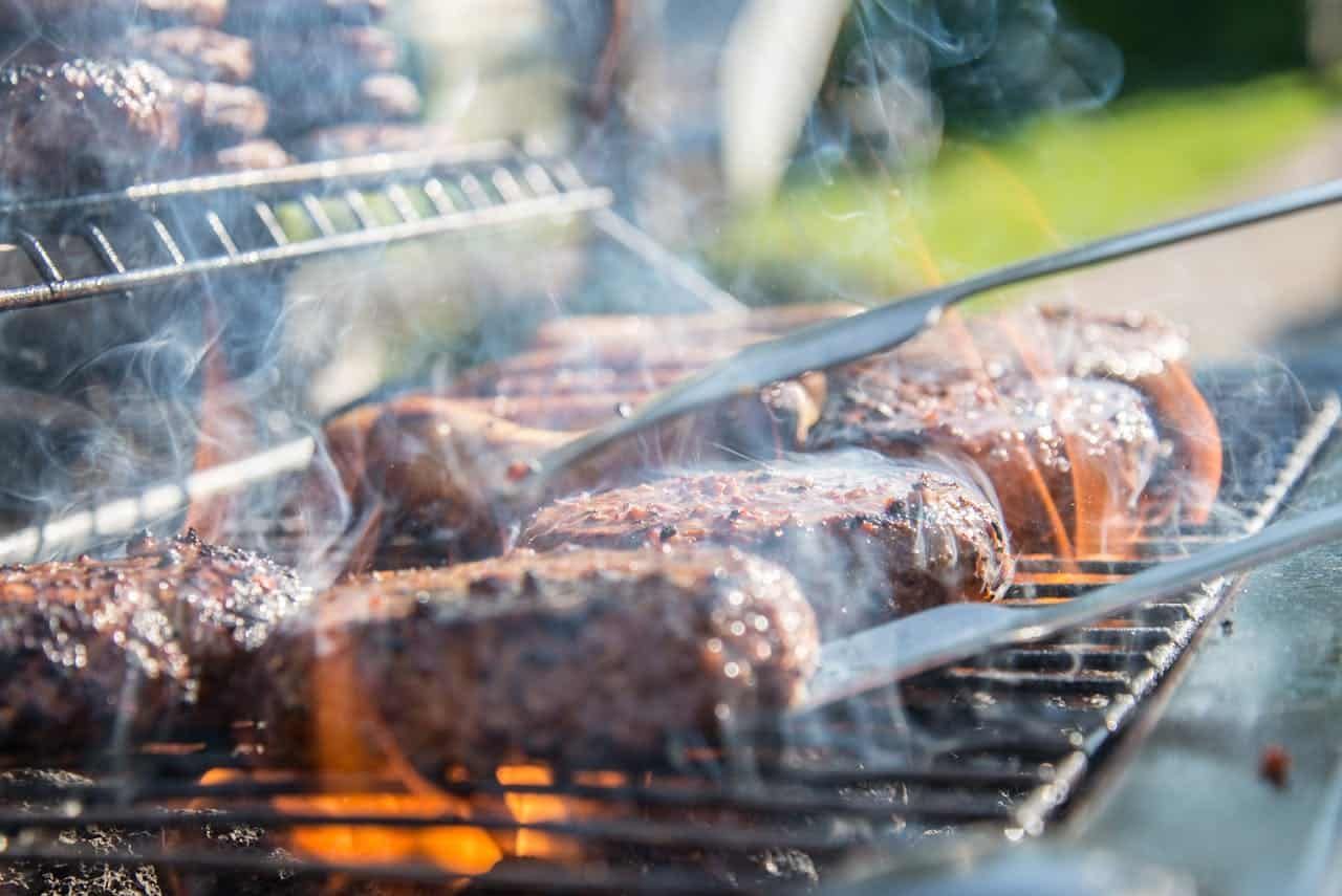 Steaks grilling on a barbecue, with tongs turning meat over glowing charcoal smoke
