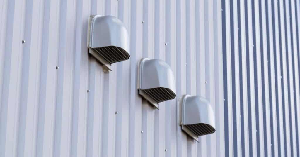 Three silver wall-mounted vents on a white corrugated metal wall