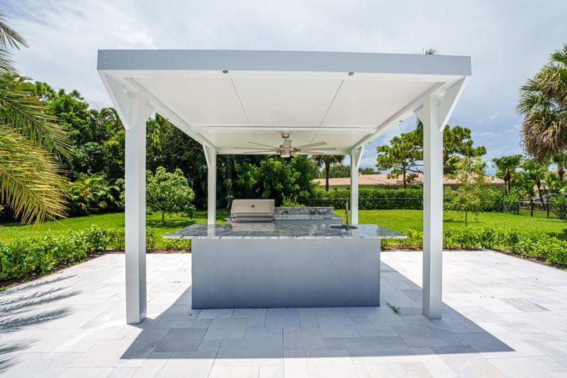 White outdoor cabana with a built-in grill in a sunny tropical garden