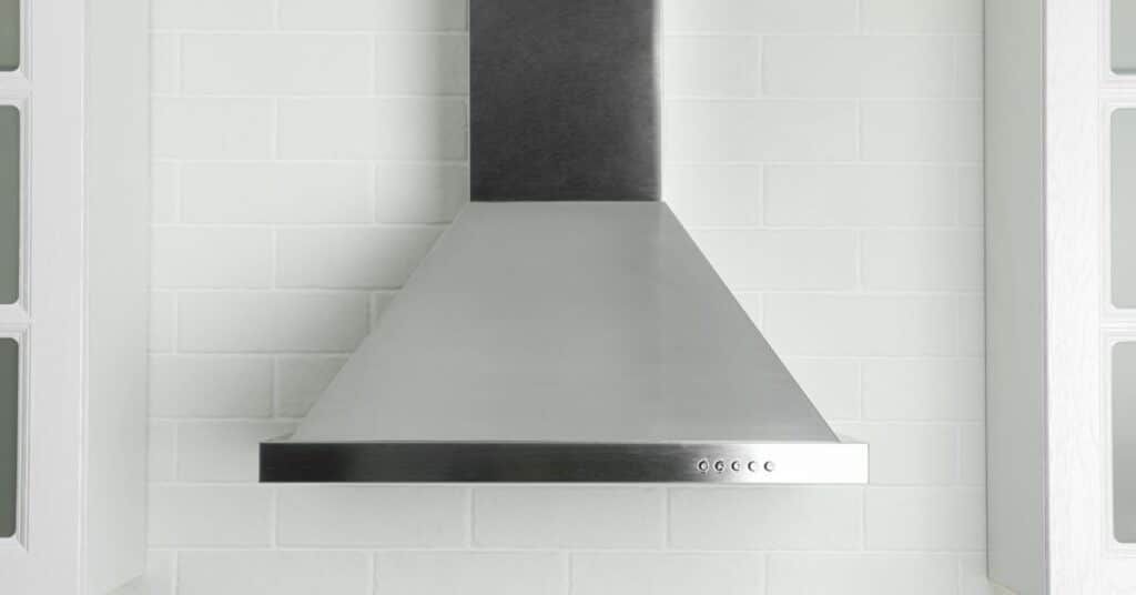 Stainless steel kitchen range hood mounted on a white tiled wall.