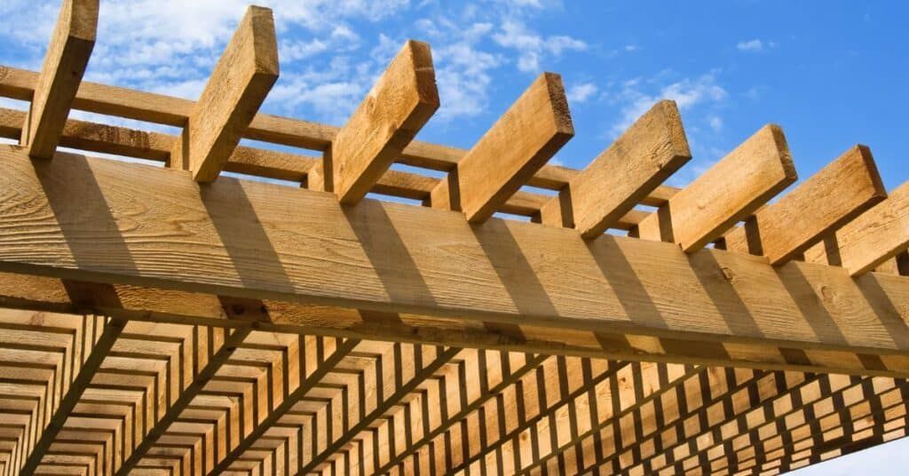 Wooden pergola beams casting repeating shadows against a bright blue sky