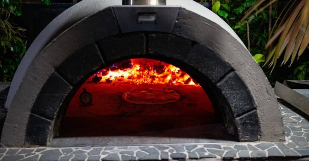 Stone pizza oven with glowing fire inside and a dark arched opening outdoors