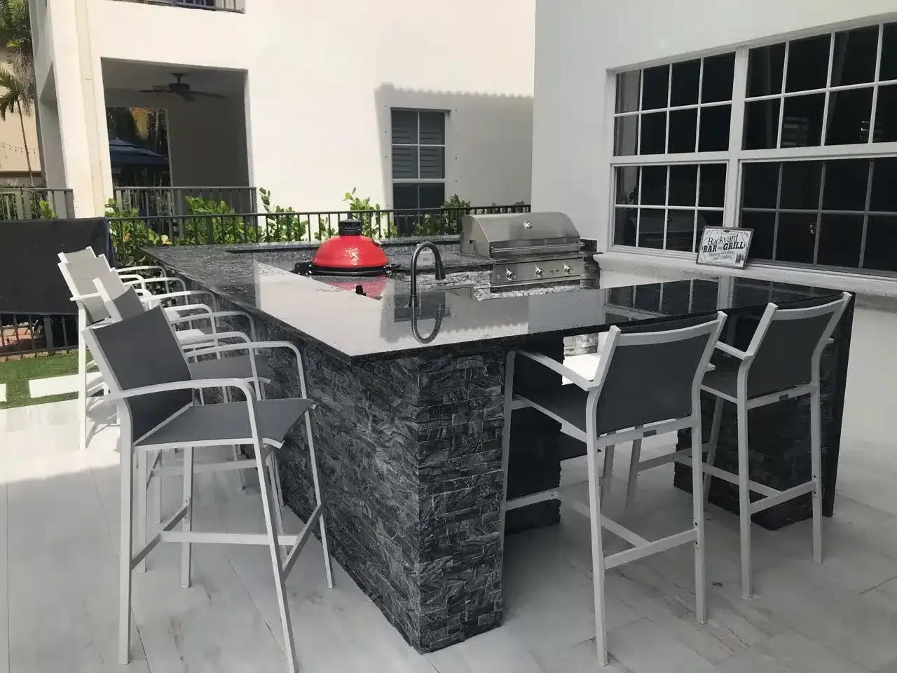 Outdoor patio dining table with black countertop, metal chairs, and a red grill in a courtyard