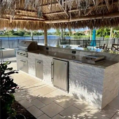 Outdoor covered patio with a built-in stainless steel grill and countertop by the pool.