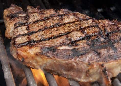 Grilled steak with char marks cooking over open flames on a barbecue grate