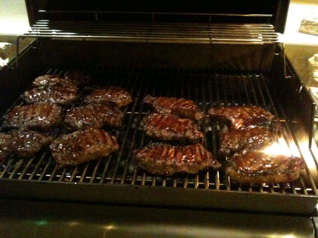 Grill with several burgers cooking over open flames on a barbecue grate