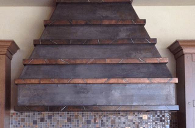 Rustic, tiered range hood with copper trim above tiled backsplash.