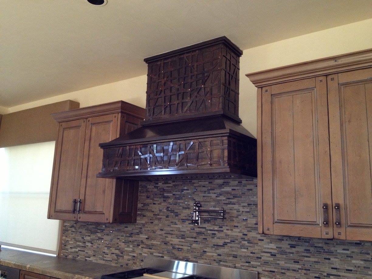 Dark wooden range hood with detailed carvings, between wood cabinets, over a tiled backsplash.