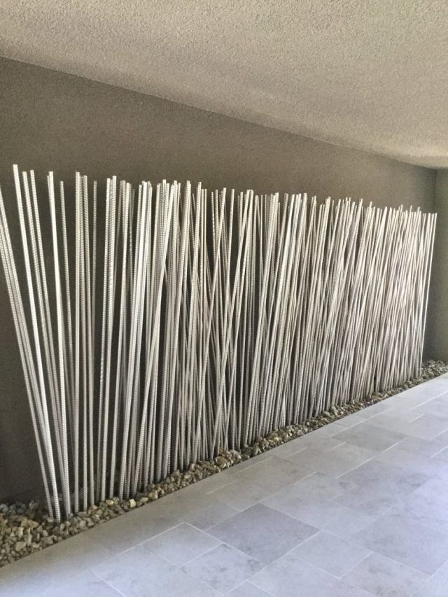 Gray wall with vertical, textured bamboo stalks forming a decorative screen; gravel and stone floor.