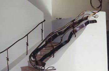 Staircase with ornate metal handrail and a simple, dark metal handrail against a white wall.