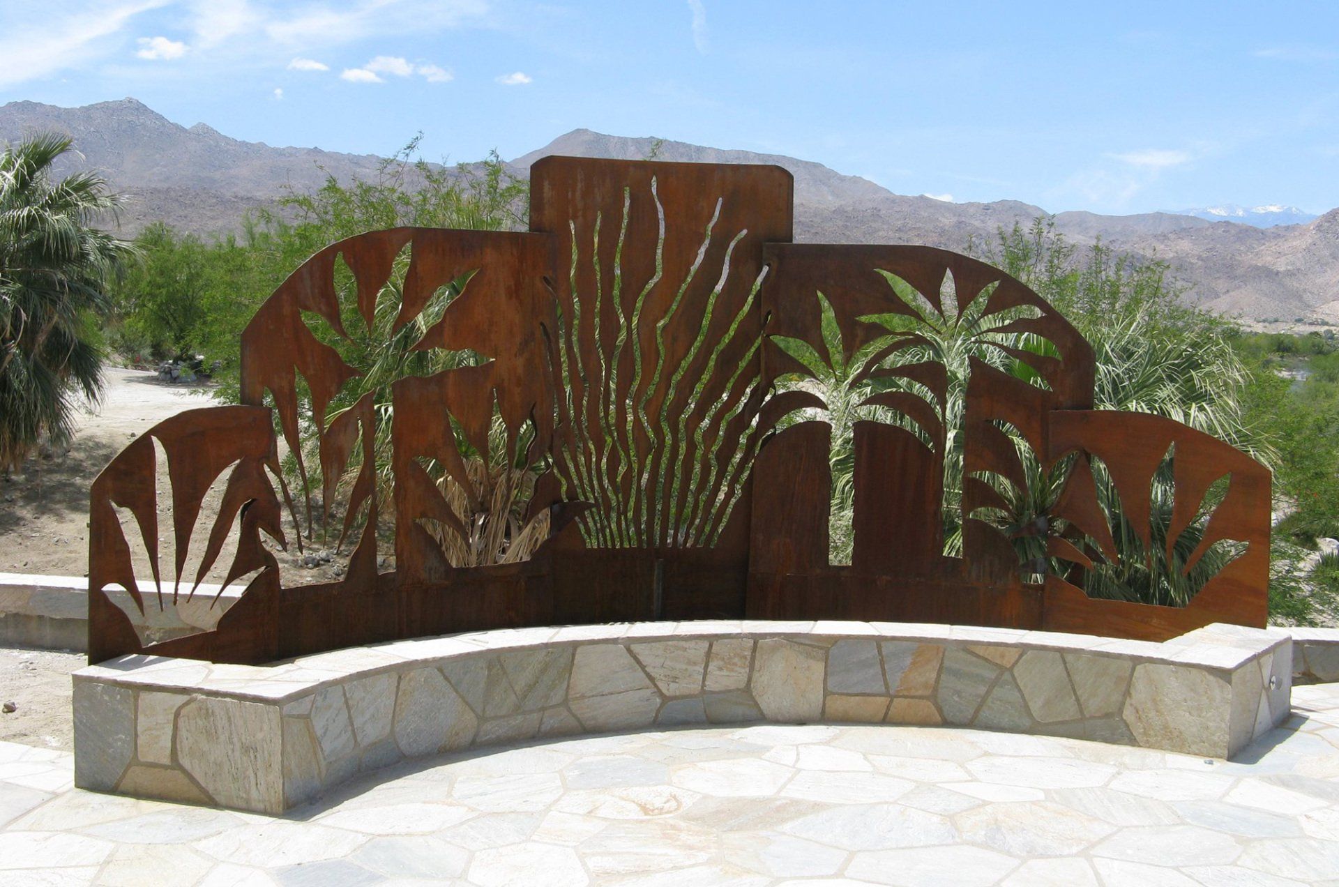 Metal art installation of desert plants in front of a mountain range.