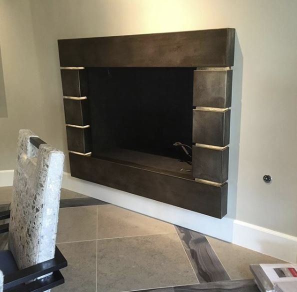 Brown, rectangular fireplace inset into a light-colored wall with a decorative art piece in the foreground.