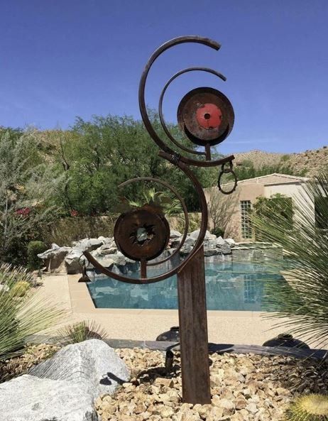 Metal sculpture in a garden with a pool and desert landscape in the background.