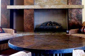 Rustic fireplace with stacked logs, flanked by textured walls and a round, dark-colored table.