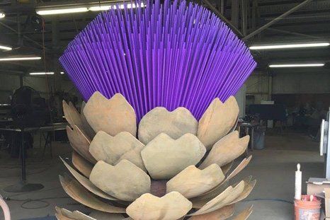 Metal sculpture of a purple thistle bloom with large tan petals in a workshop.