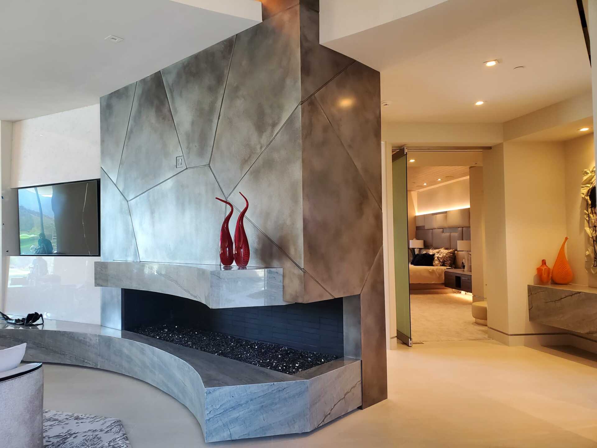 Modern fireplace with grey, geometric design and glass embers; two red vases.