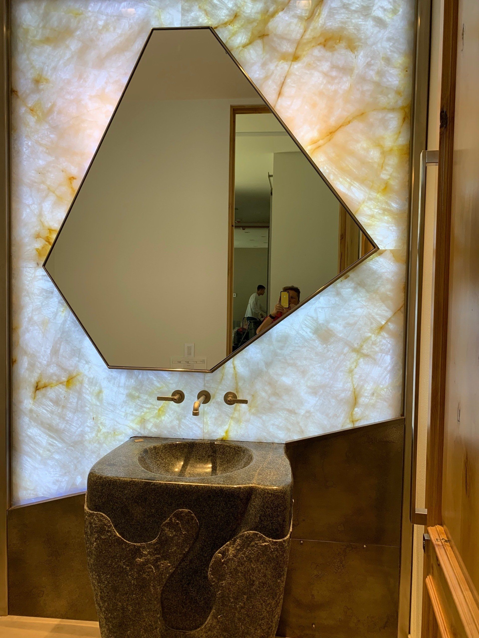 Bathroom with a stone pedestal sink, asymmetrical mirror, and backlit onyx wall.