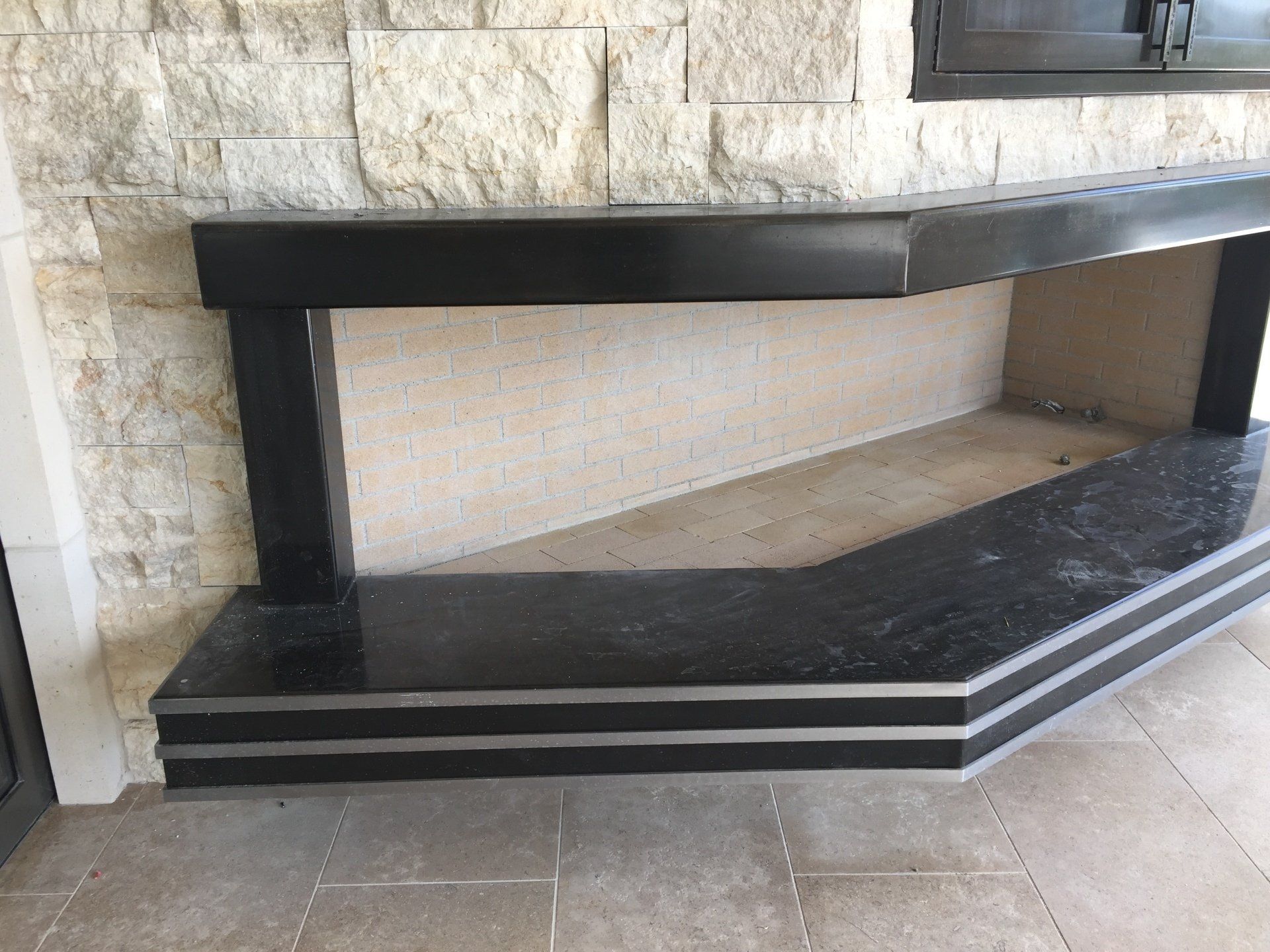 Outdoor black granite fireplace with a white stone wall background.