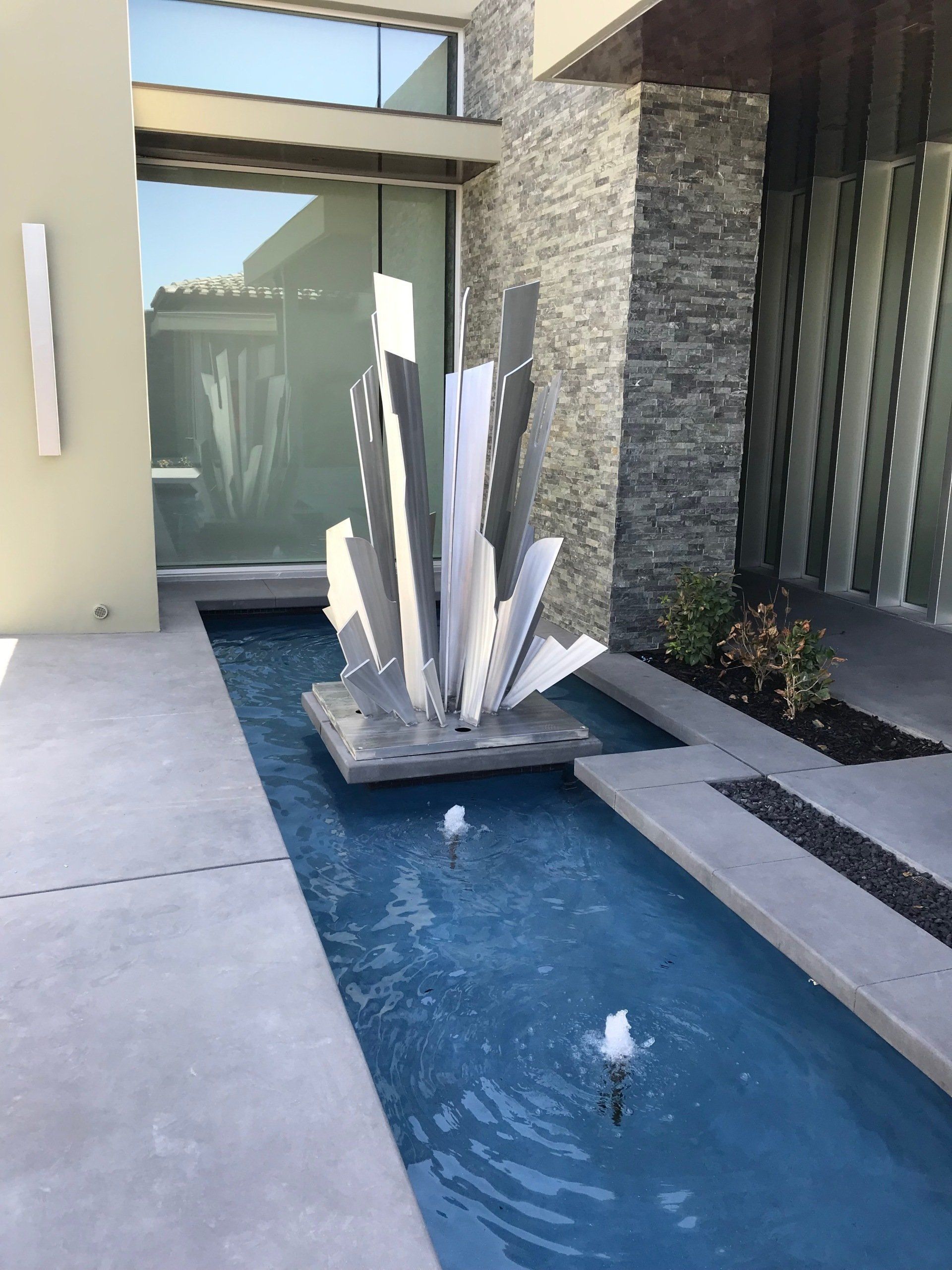 Modern water feature with sculpture in a shallow pool; contemporary architecture.