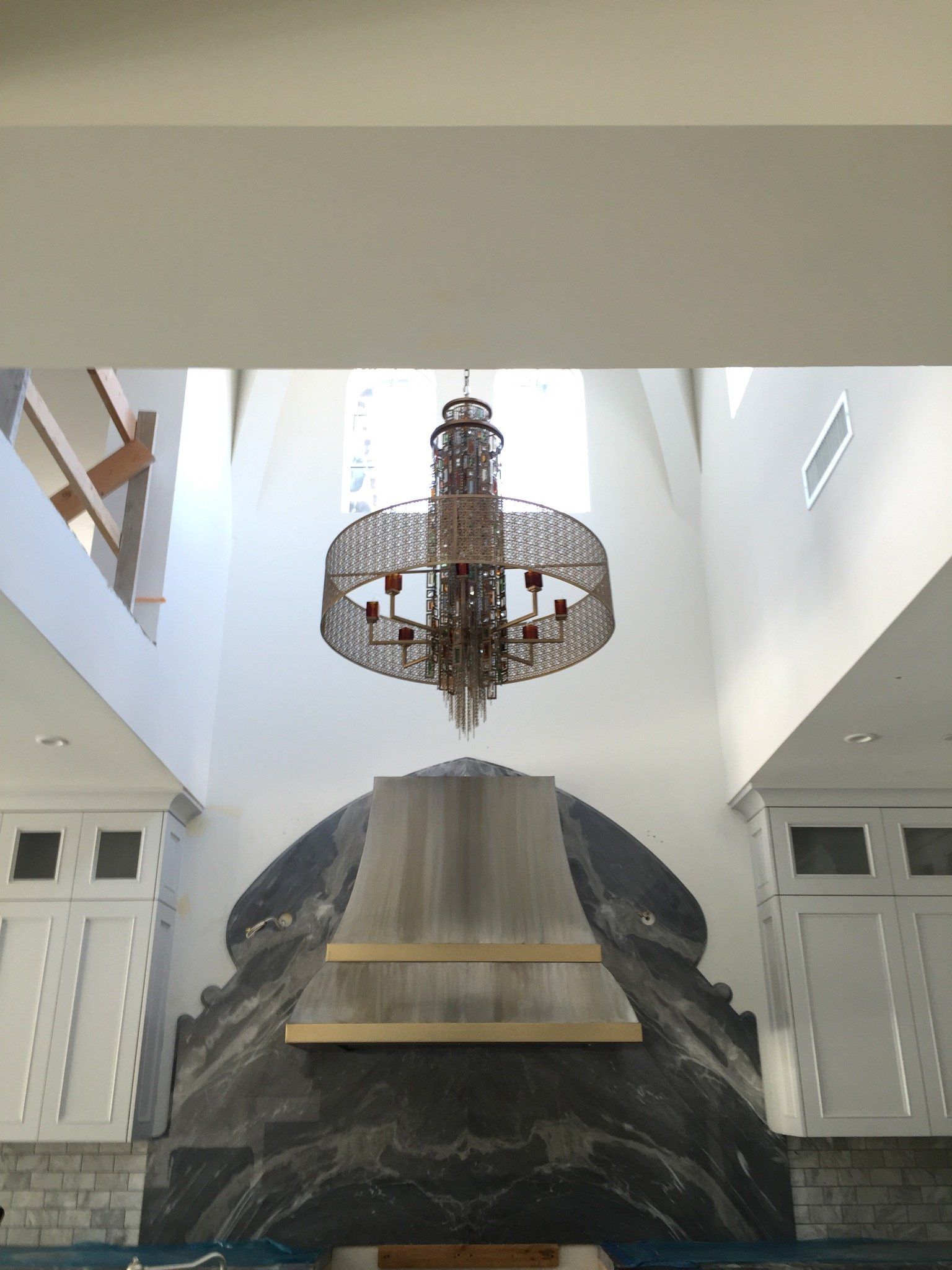 Ornate chandelier hangs above a large dark stone fireplace in a white room.