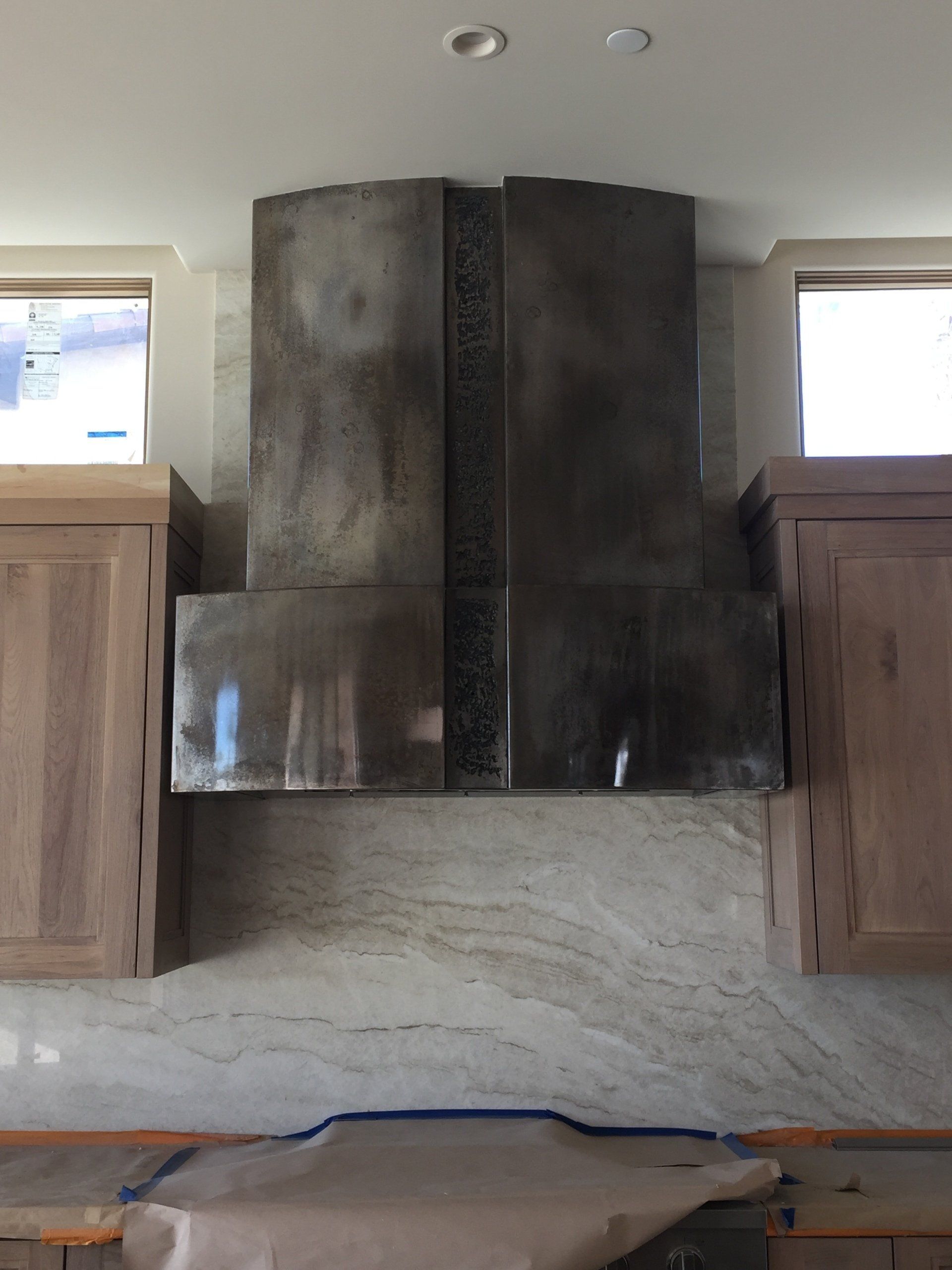 Stainless steel range hood centered between wooden cabinets, over granite countertop.