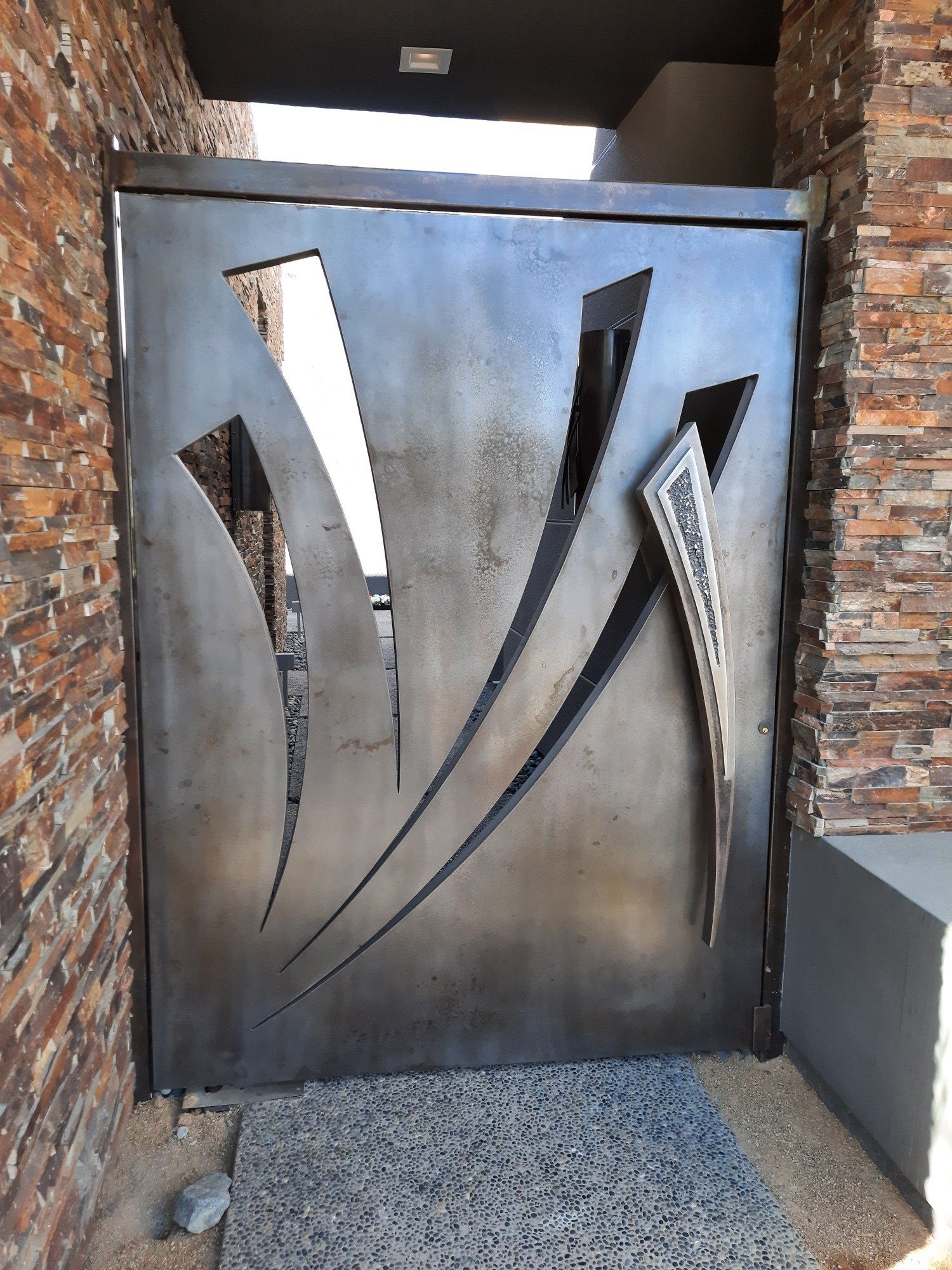 Metal gate with abstract cutouts; in front of a brick wall.