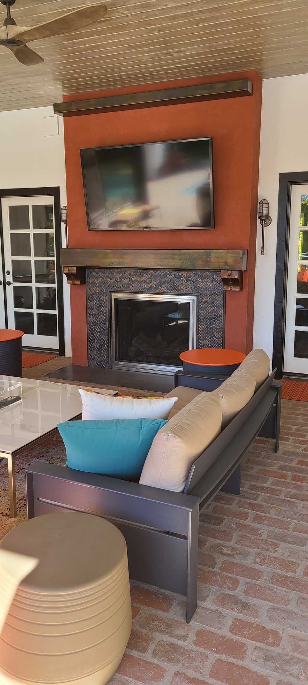Outdoor living room with a fireplace and TV; seating area with cushions.