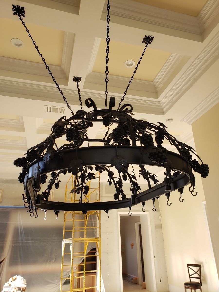 Large black wrought iron chandelier with grape leaf and vine details, hanging in a room with scaffolding.