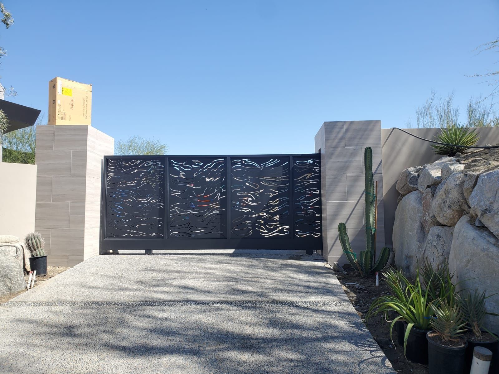 Black metal driveway gate with an ornate design, between stone pillars.