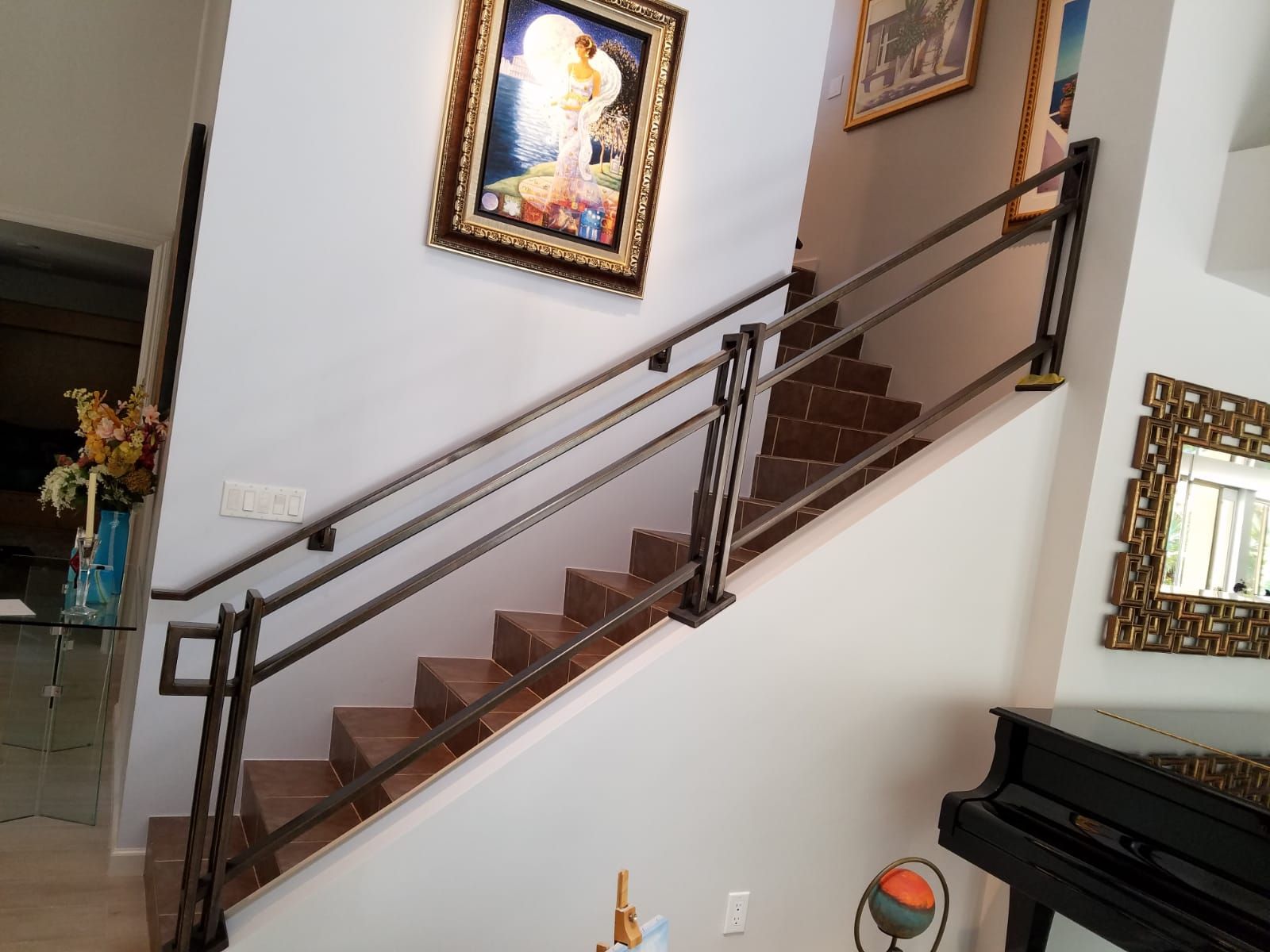 Staircase with metal railing, framed art, and a piano in a well-lit home.