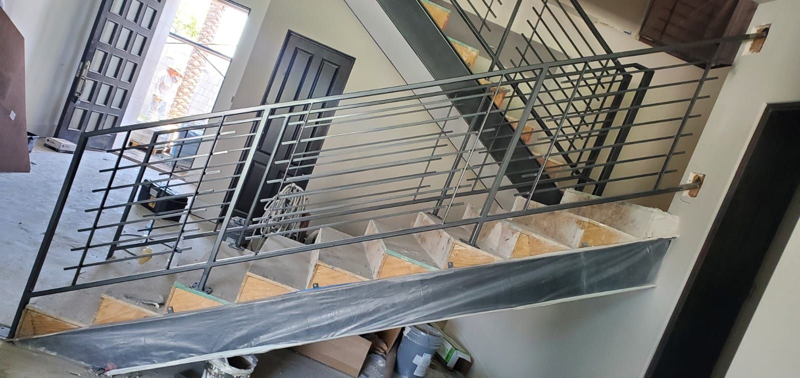 A staircase with a black metal railing is being constructed in an indoor setting.
