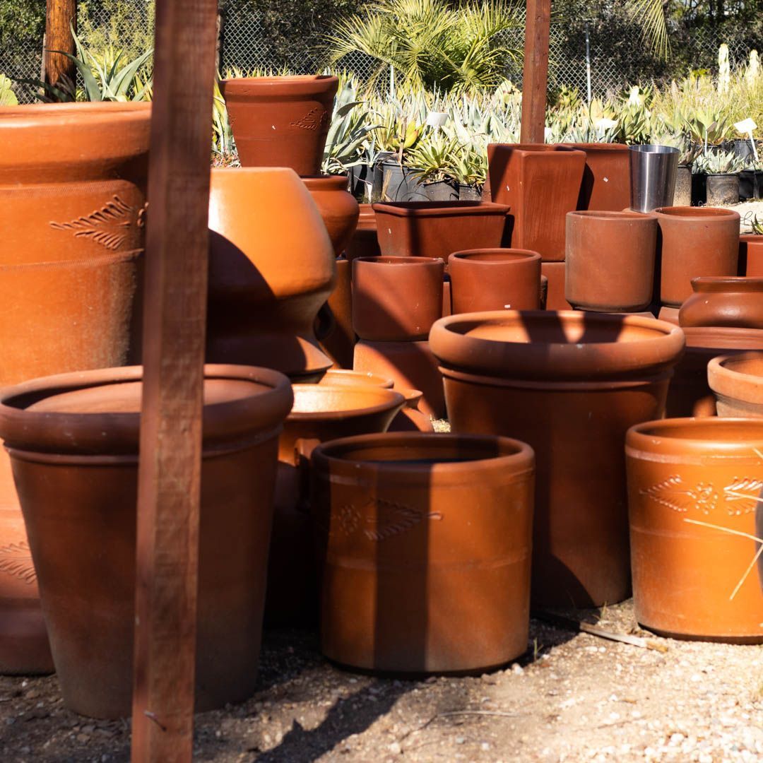 Pile of terracotta plant pots in a nursery, with various shapes and sizes, outdoors.